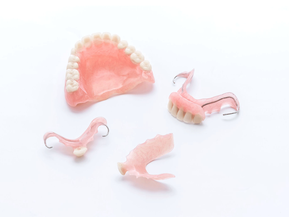 Various types of dental prosthetics displayed on a white background, including a partial denture, orthodontic retainers, and a dental bridge. Each piece is designed to fit precisely, showcasing the art and precision of modern dental restoration.