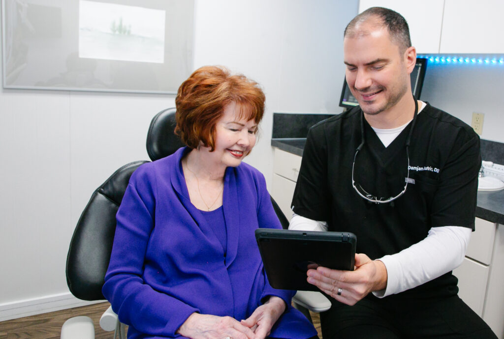 a dentist shows an older female patient images of her teeth on a tablet