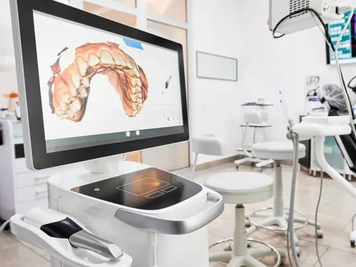 Modern dental clinic featuring a computer monitor displaying a detailed 3D dental scan. The clinic is equipped with advanced dental technology, including dental chairs and various instruments, highlighting a high-tech environment for comprehensive dental care.
