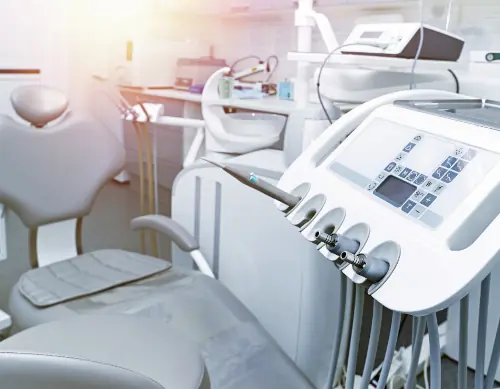 Brightly lit dental clinic showing a dental chair with attached tools and equipment console, featuring various handpieces and digital controls.